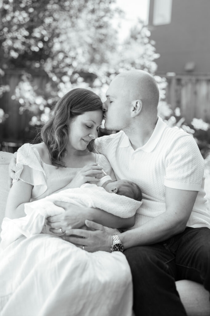 new father leans in to kiss new mother - first time parents with their newborn during a Bay Area newborn photography session