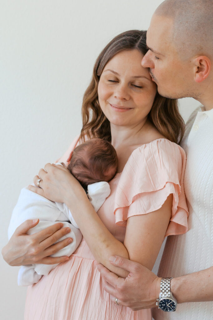new parents hold newborn baby while new dad kisses new mom's forehead during their in home newborn photography session in San Francisco