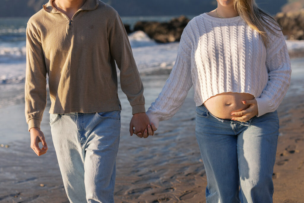 San Francisco maternity photographer capturing couple walking along Baker Beach at sunset