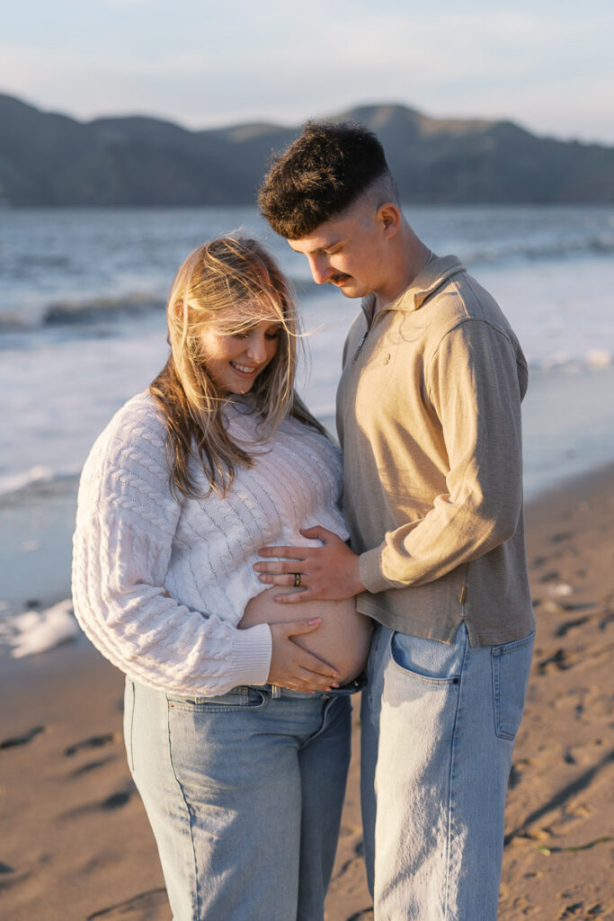 Expecting parents holding baby bump during Baker Beach maternity session