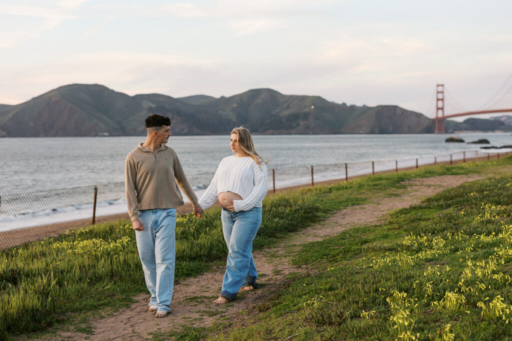 San Francisco maternity photographer capturing couple walking along Baker Beach at sunset