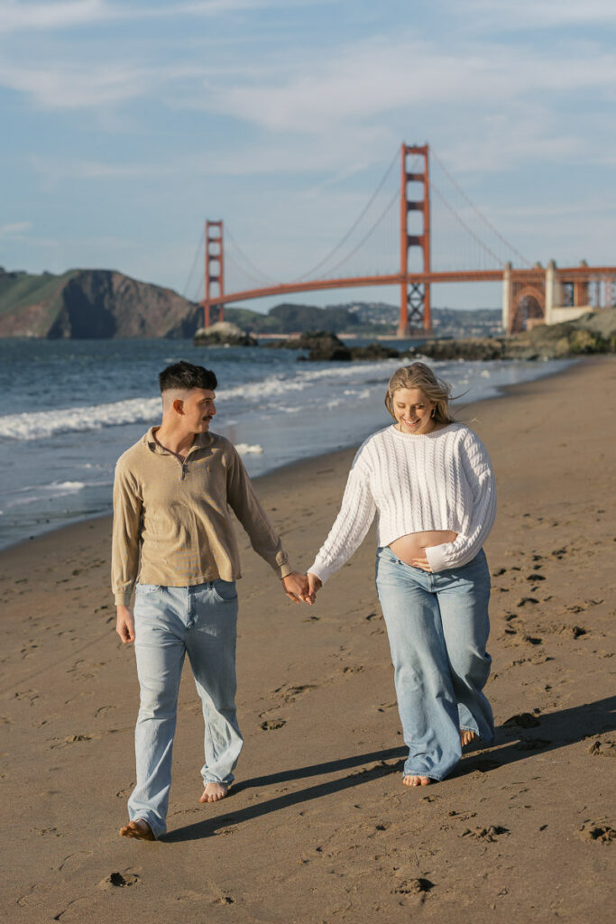 San Francisco maternity photographer capturing couple walking along Baker Beach at sunset