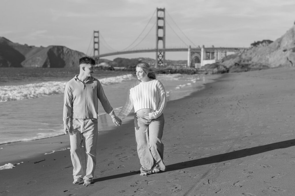 San Francisco maternity photographer capturing couple walking along Baker Beach at sunset