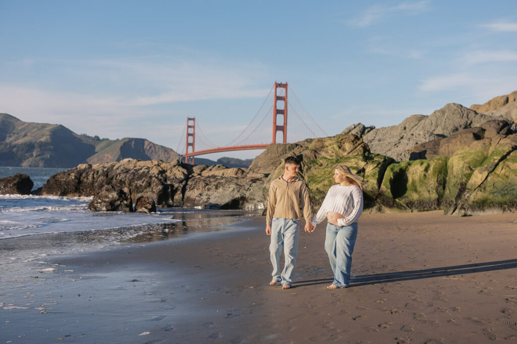 San Francisco maternity photographer capturing couple walking along Baker Beach at sunset
