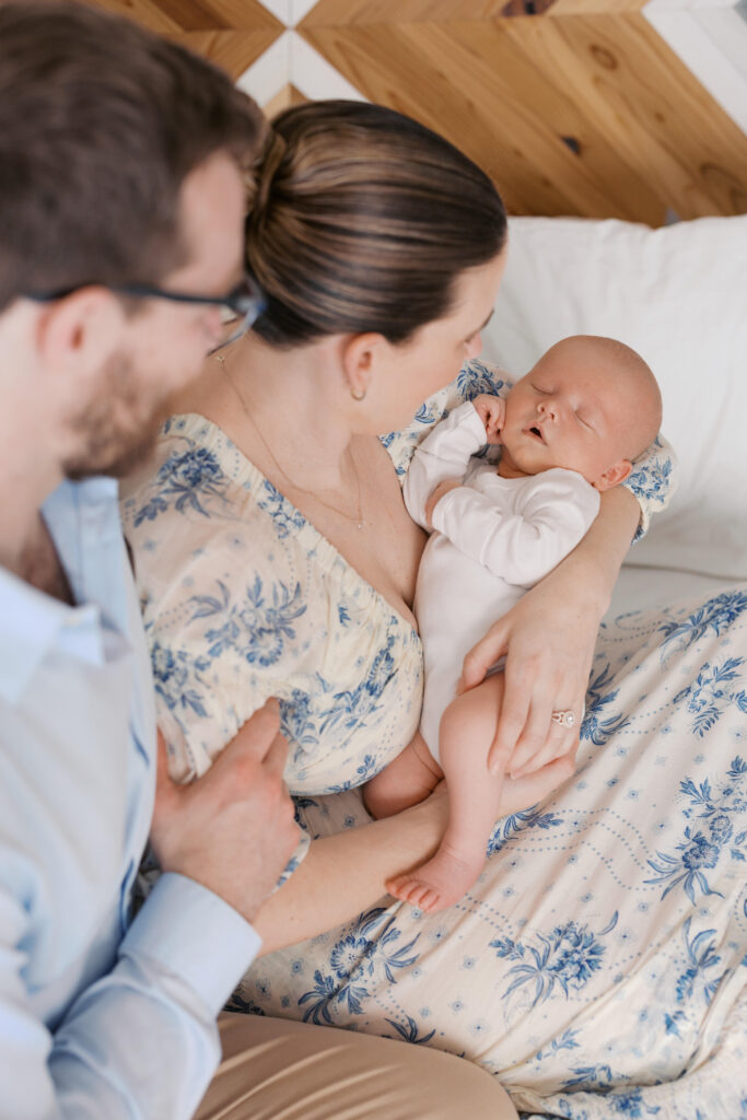first time parents hold newborn baby boy while siting on a white bed during East Bay newborn photography session in Oakland