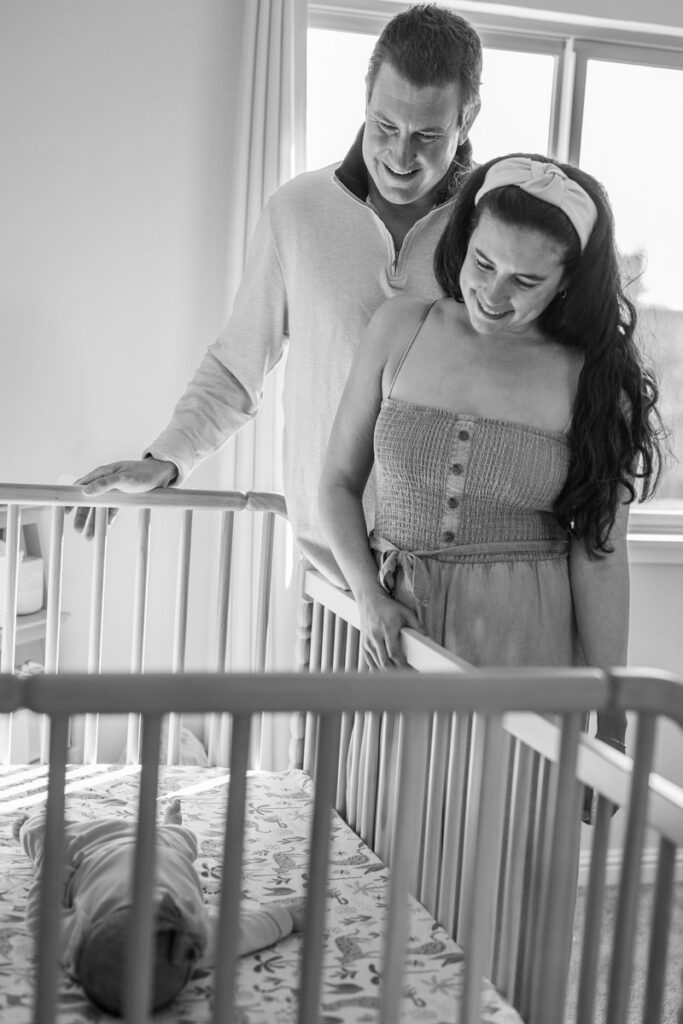 parents gaze down at 2 month old newborn in crib