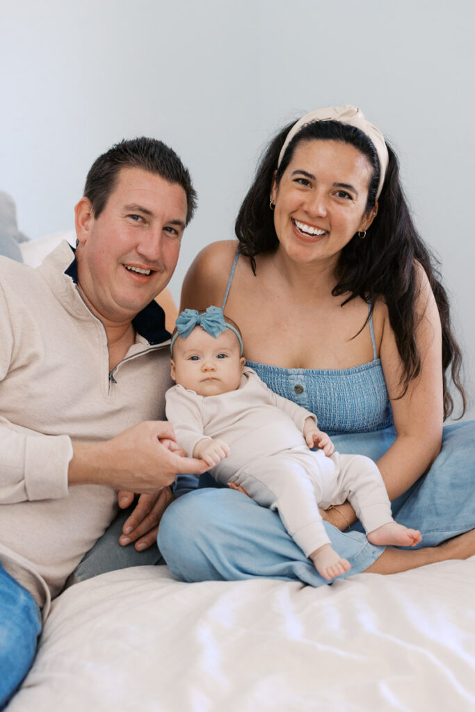 new parents smile and sit on bed with 2 month old baby girl during in home newborn photography session in Bay Area