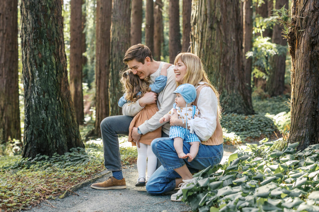 family of four hug and laugh in redwood grove at Berkeley Botanical Garden during Berkeley family photography session