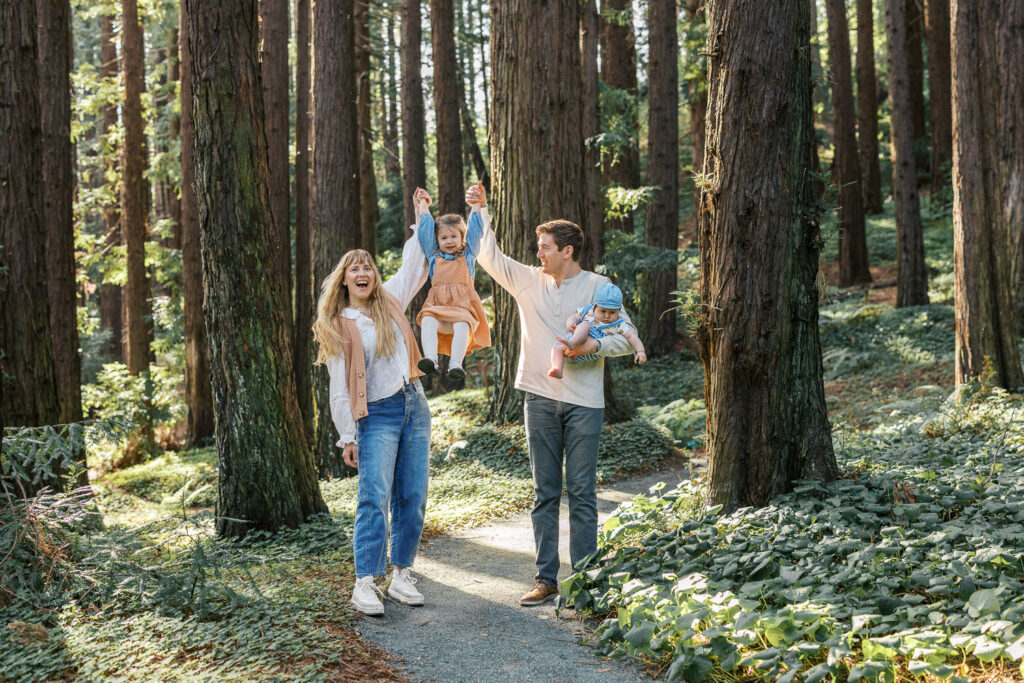 parents lift two year old in the air while holding baby brother in the redwoods during Berkeley family photography session