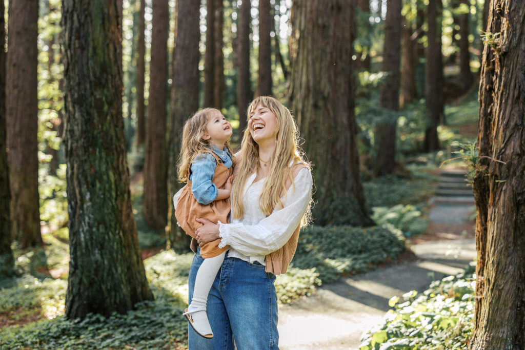 mom and toddler daughter laugh in the redwood grove at Berkeley Botanical Garden