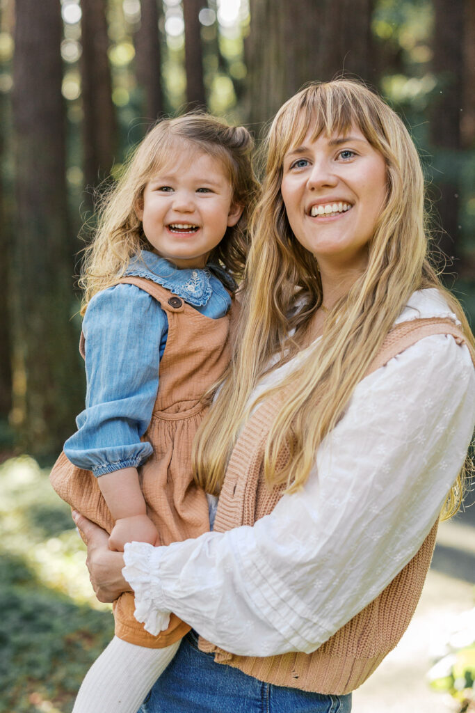 mom holds toddler daughter in redwoods in Berkeley as they both laugh during their Bay Area family photography session