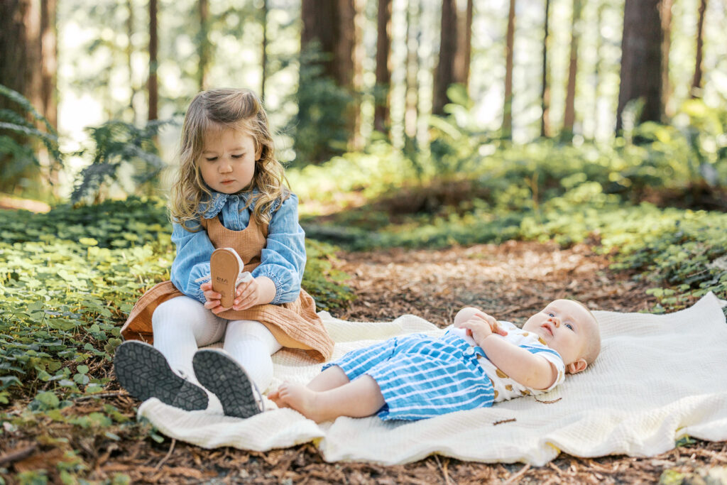 toddler big sister and baby brother lay on a blanket in the redwood grove at Berkeley Botanical Garden during Berkeley family photography session