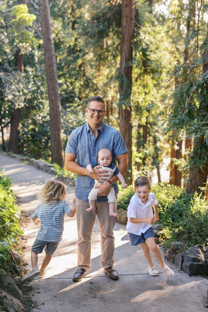 dad with three young boys, the oldest two run around him while he holds the baby at Dracena Park