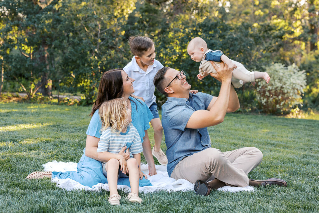 family of five sits on blanket at Dracena Park watching as dad lifts baby during Piedmont family photography session