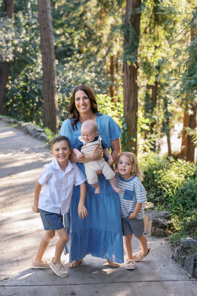 mom holds baby and two older brothers are on each side of her - mom of three. all smile at camera during a piedmont family photography session at dracena park