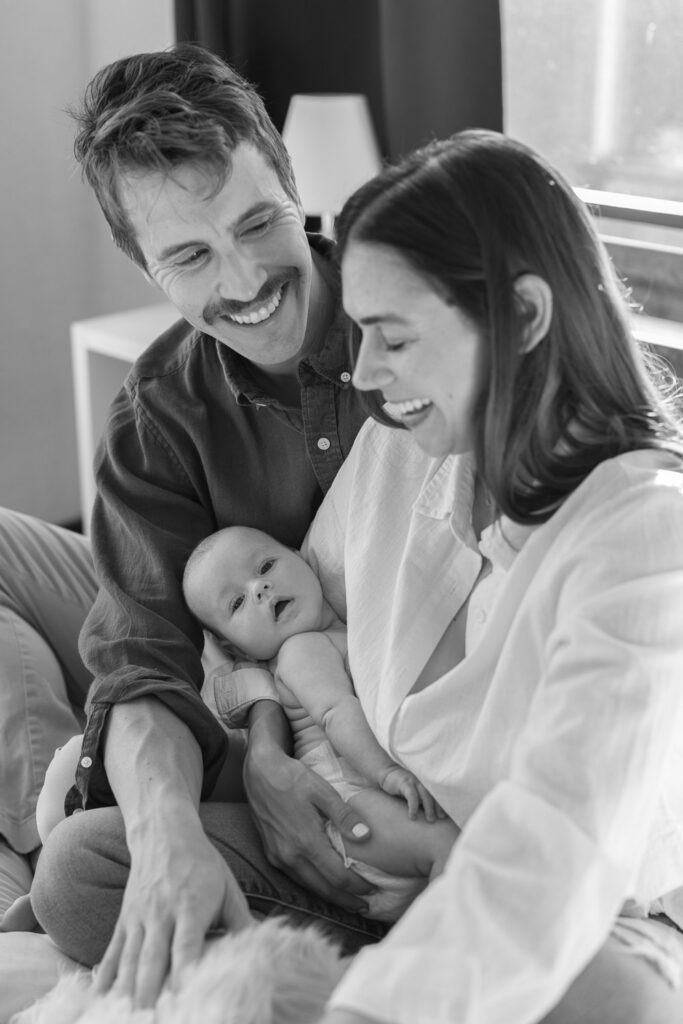 new dad gazes at his wife while she laughs and holds their 2 month old newborn during San Francisco newborn photography session