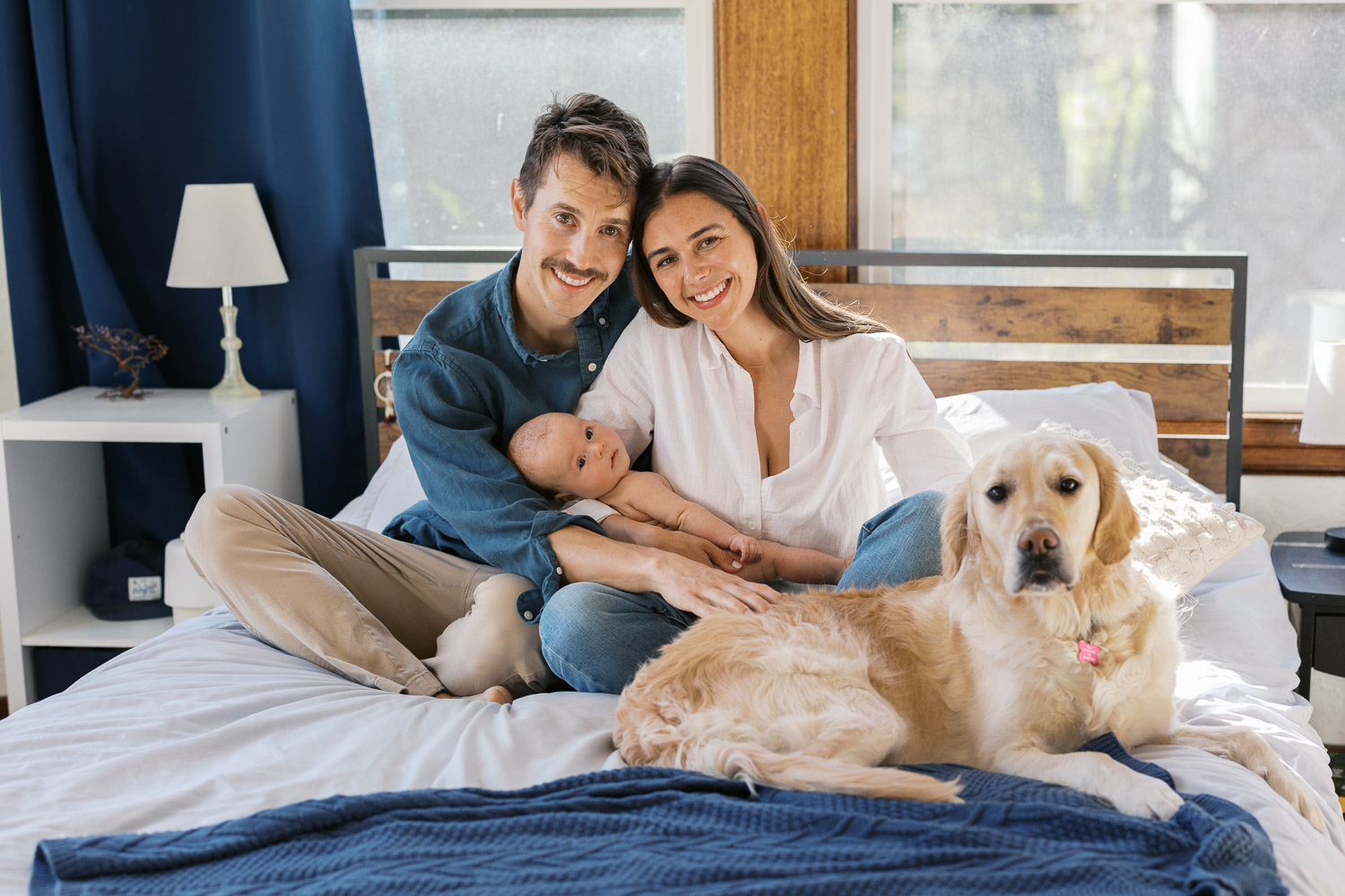 new parents hold newborn while sitting on bed with dog for San Francisco newborn photography session