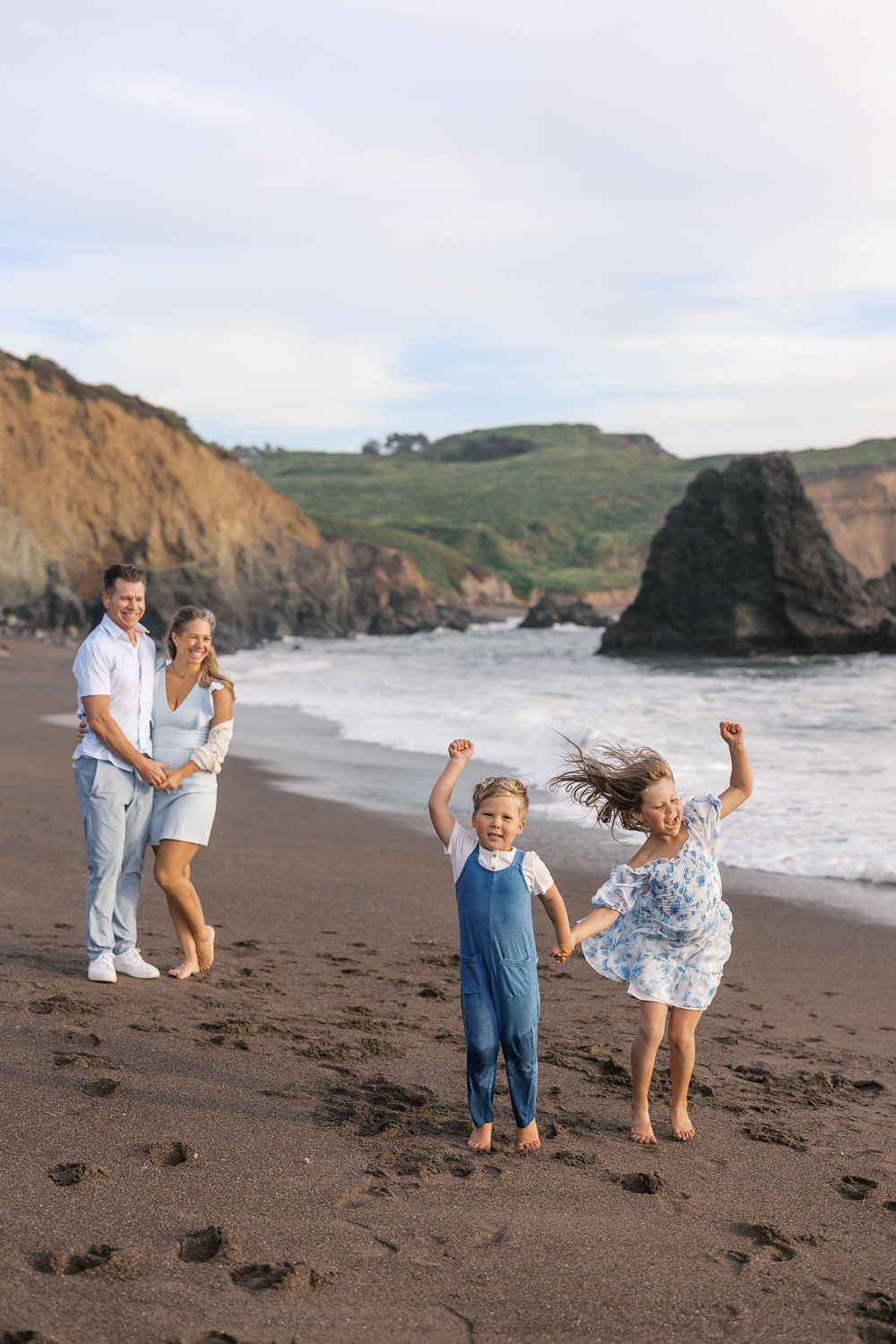 family of four play on rodeo beach in marin county - parents snuggle and watch as two young children dance