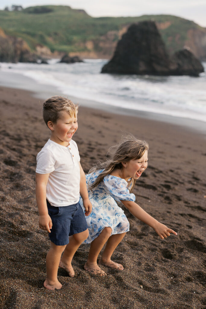 two young children laughing hard while on rodeo beach in marin county