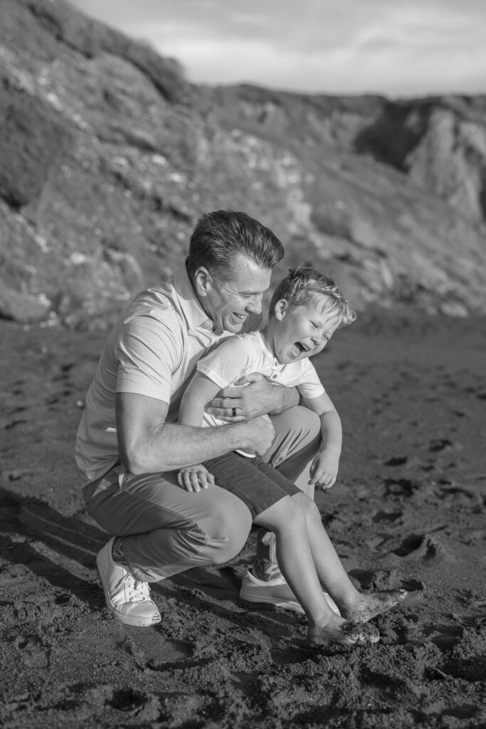 dad holds son, both laughing, during rodeo beach family photography session