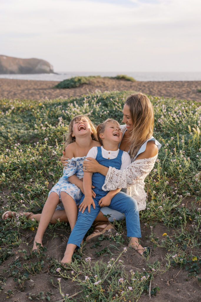 mom holds two young children while they all laugh on rodeo beach