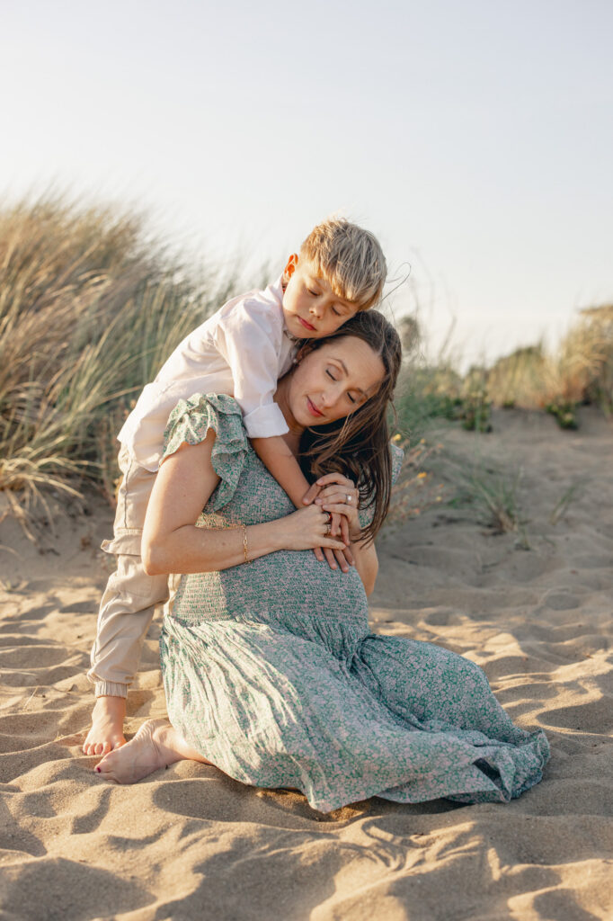 Son hugs expecting mom from behind at golden hour at Alameda Beach during an East Bay Area maternity photography session