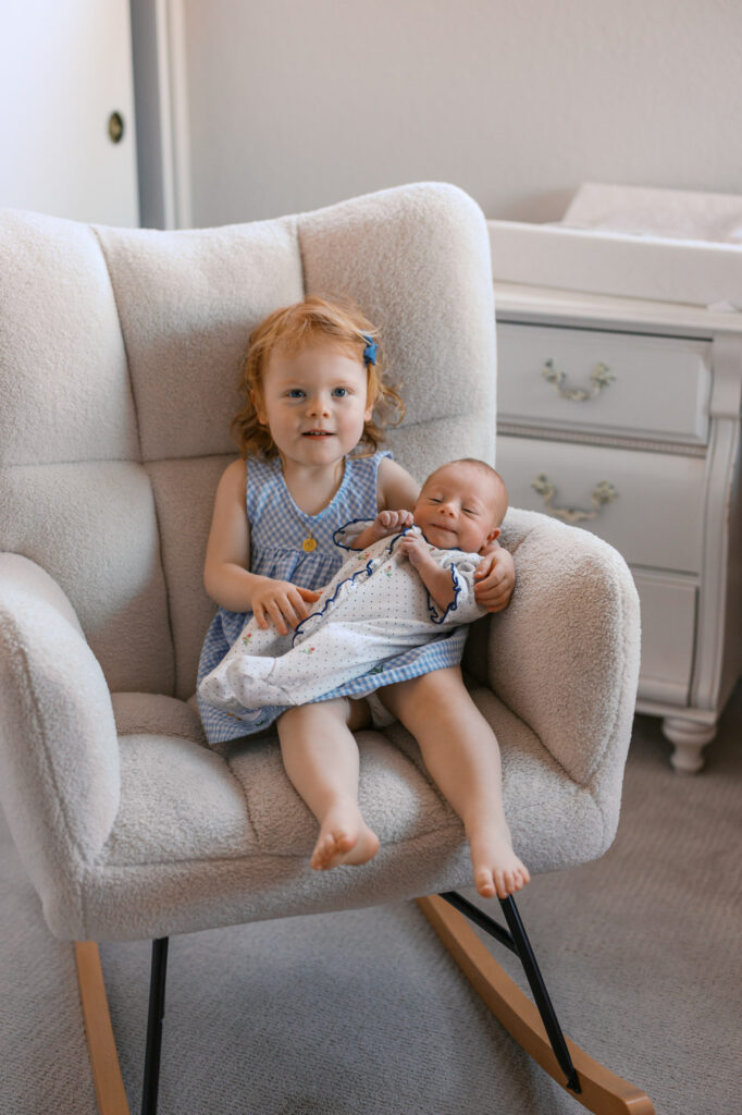toddler big sister holds newborn baby sister and smiles during an Alameda newborn photography session