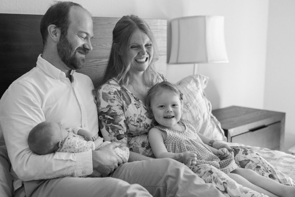 family of four laugh on the bed during newborn session
