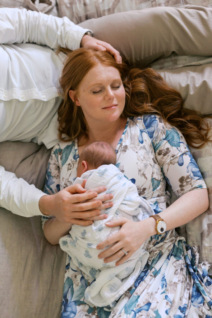 mom rests on dad while holding newborn baby girl during Alameda newborn photography session