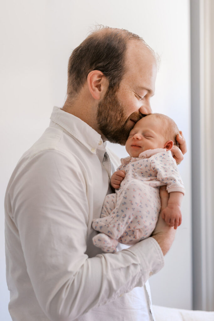 dad kisses newborn baby girl during Alameda in home newborn session