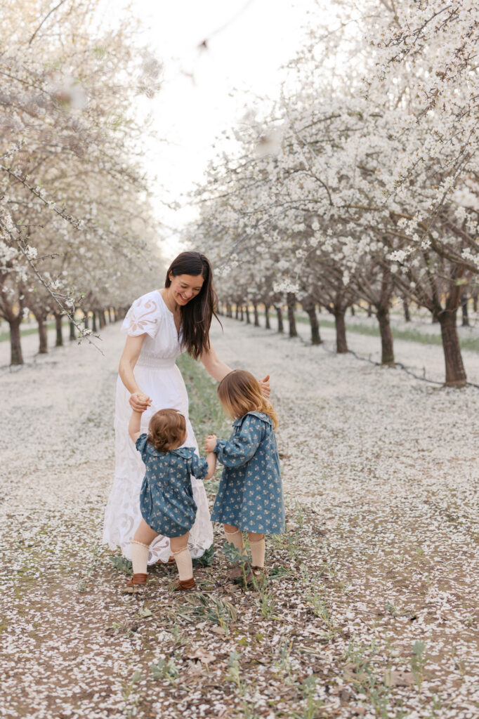 Bay Area family photographer Rebecca Pattison dances with her two daughters in the almond tree grove in Yolo County