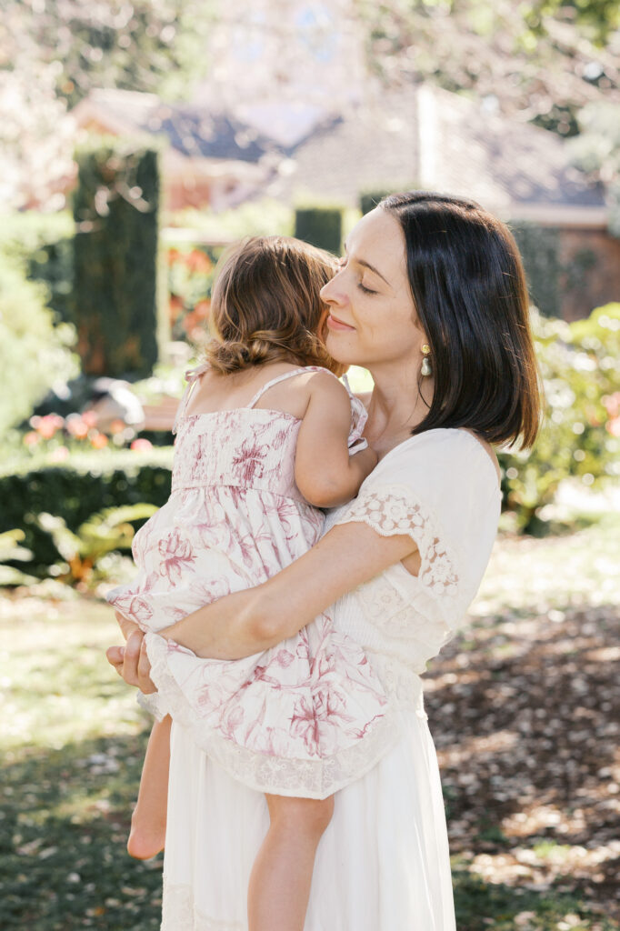 Mom in white holds onto and hugs toddler daughter at Filoli in Woodside during a Bay Area family photography session