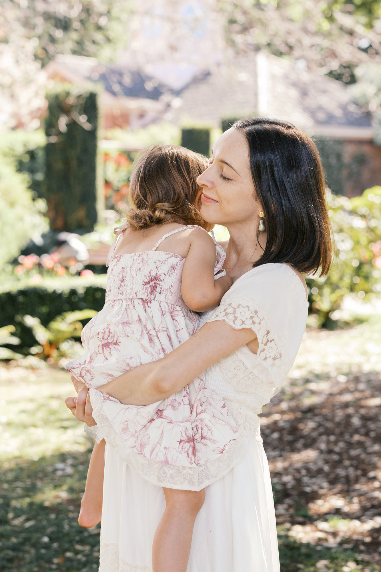 Mom in white dress holds young toddler girl while at Filoli for Bay Area maternity photos