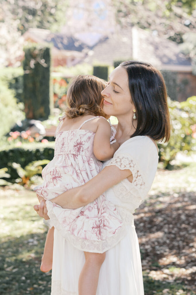mom in white dress holds and hugs toddler daughter at Filoli in Woodside during her Bay Area maternity photography session