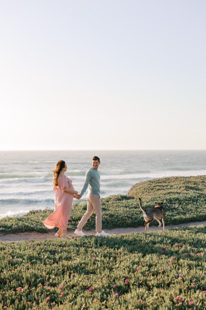 Expecting couple walk along the cliffs in Half Moon Bay with their dog during their Bay Area maternity photography session