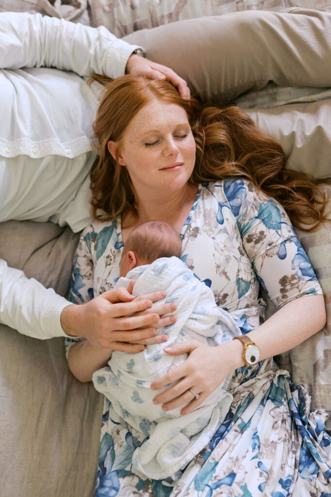 mom rests on dad while holding newborn baby girl during Alameda newborn photography session