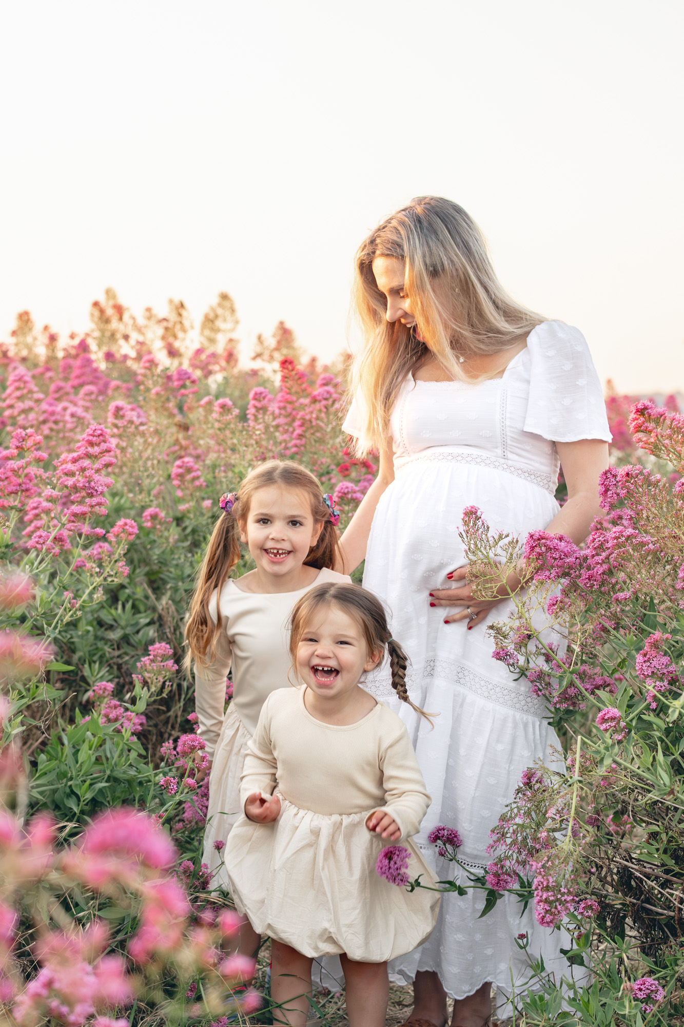 Expecting mom with her two young daughters play in a pink flower field in East Bay during Bay Area maternity photography session