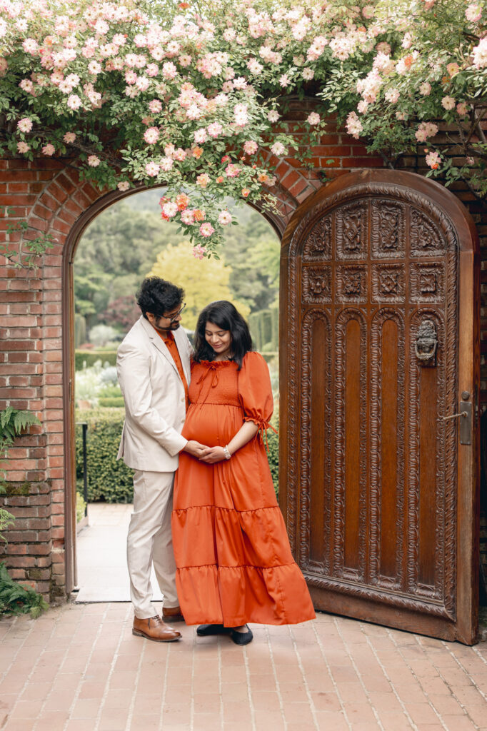 Filoli maternity session in Woodside with expecting couple standing in front of one of Filoli's main gates, gazing at mom's pregnant belly during Bay Area maternity photography session