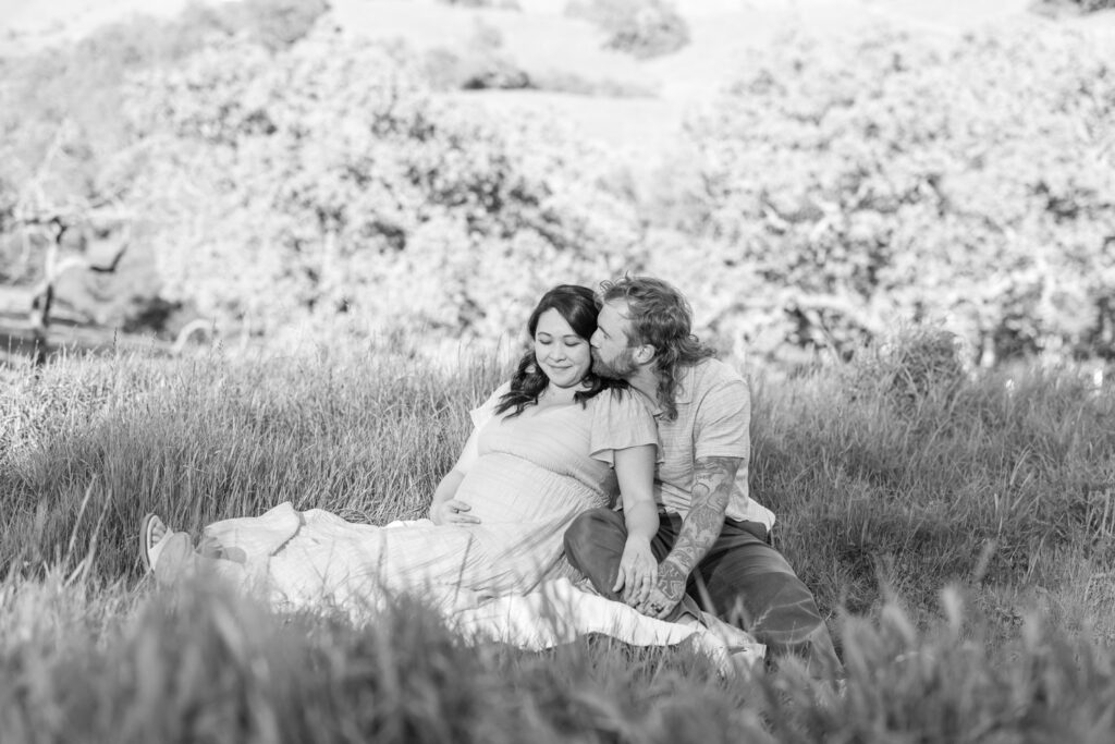 man kisses woman on the temple as she gazes down at her baby bump during their Walnut Creek maternity photography session