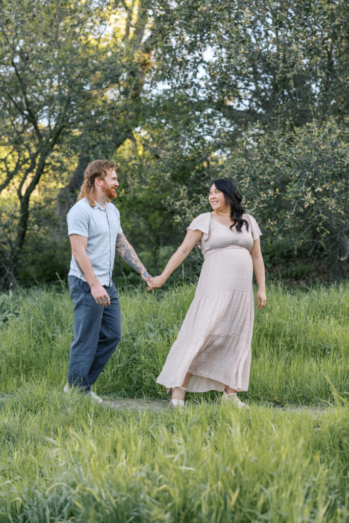 Couple walks through trees and green golden hills during Walnut Creek maternity photography session
