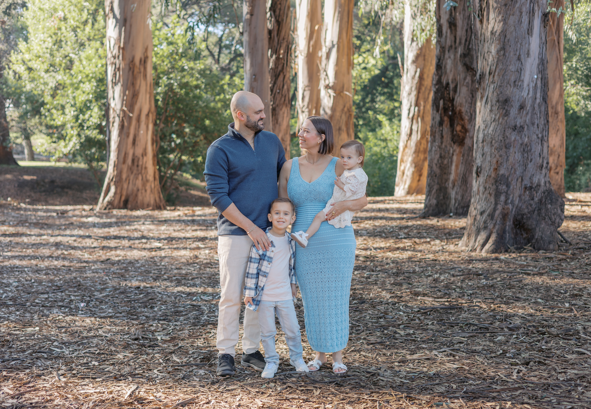 family of four in blues and neutrals stands in eucalyptus grove in Berkeley for Bay Area family photos