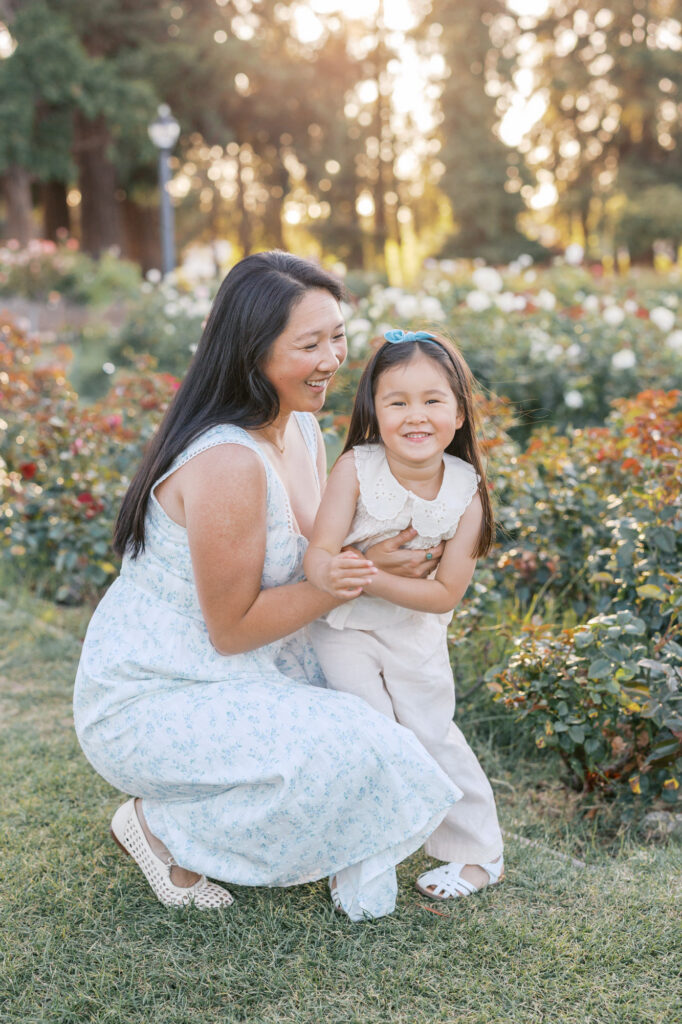 Mother and young daughter laugh and embrace near the roses during a San Jose Rose Garden photography session
