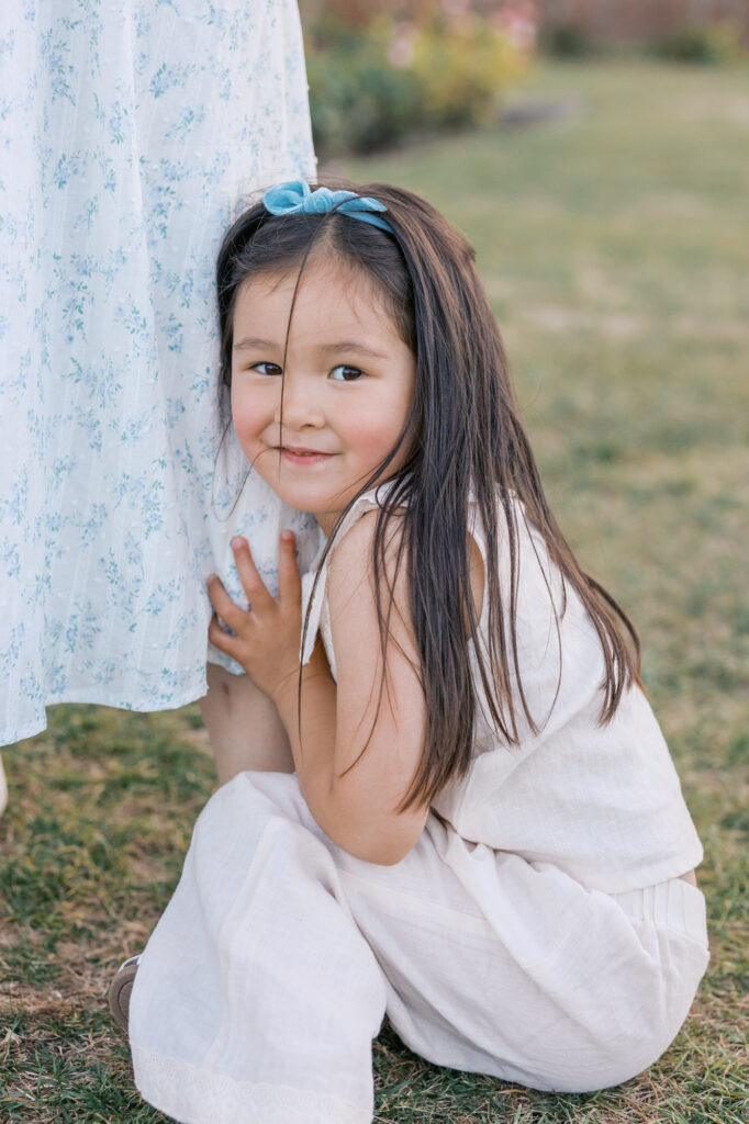 young toddler sits on the grass and holds on to mothers leg during San Jose Rose Garden photography session