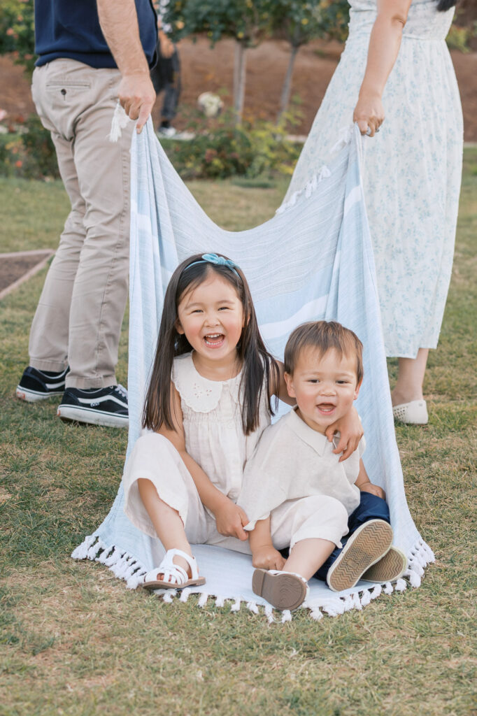 two young children sit on a blanket laughing at the San Jose Rose Garden during a Bay Area family photography session