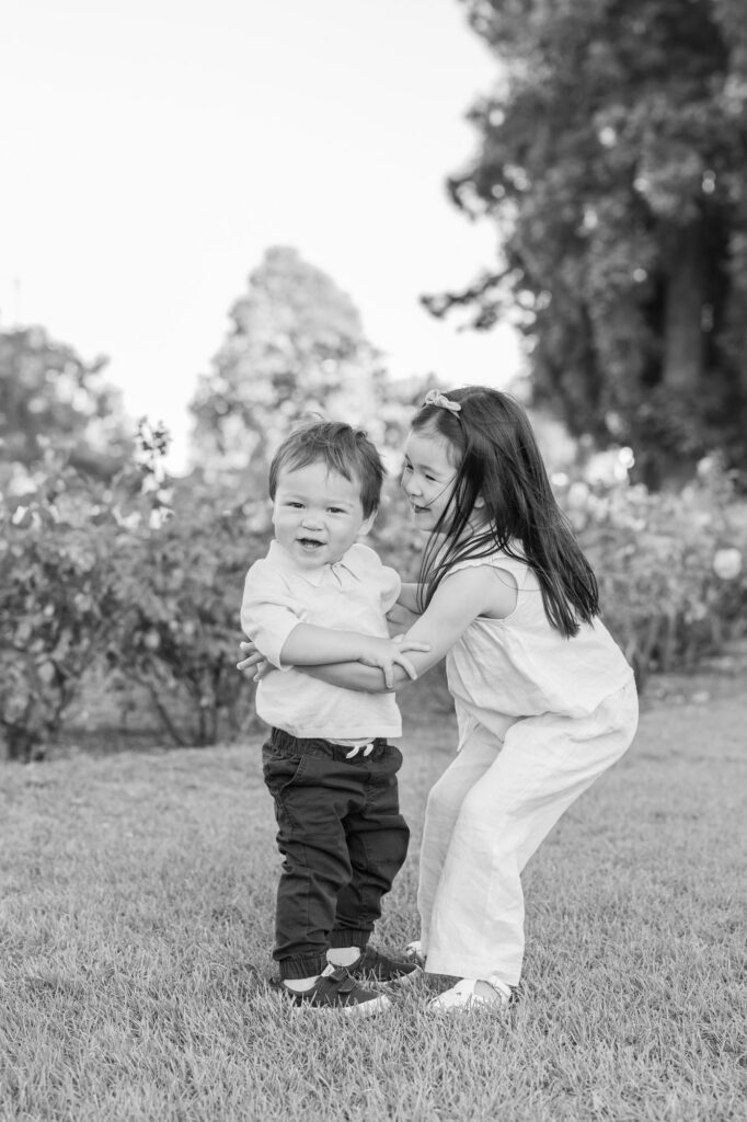 toddler sister embraces her younger brother while they both laugh at the San Jose Rose Garden
