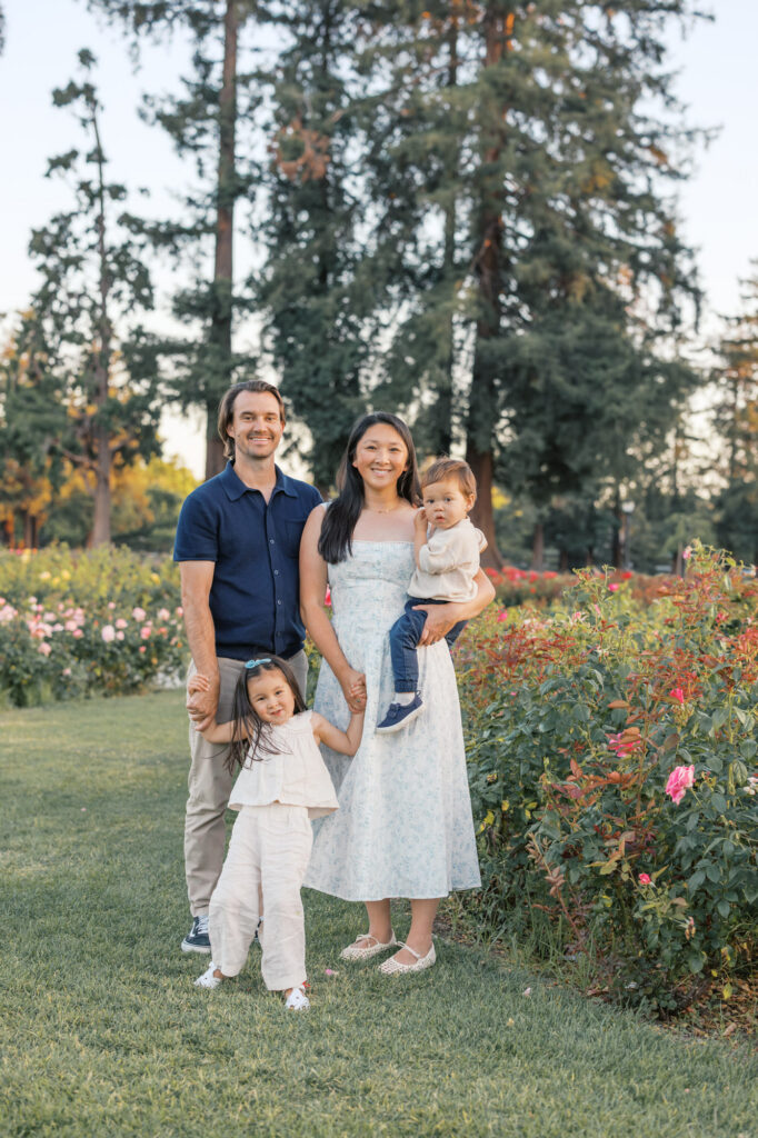 family of four smile and pose next to the roses at the San Jose Rose Garden during golden hour