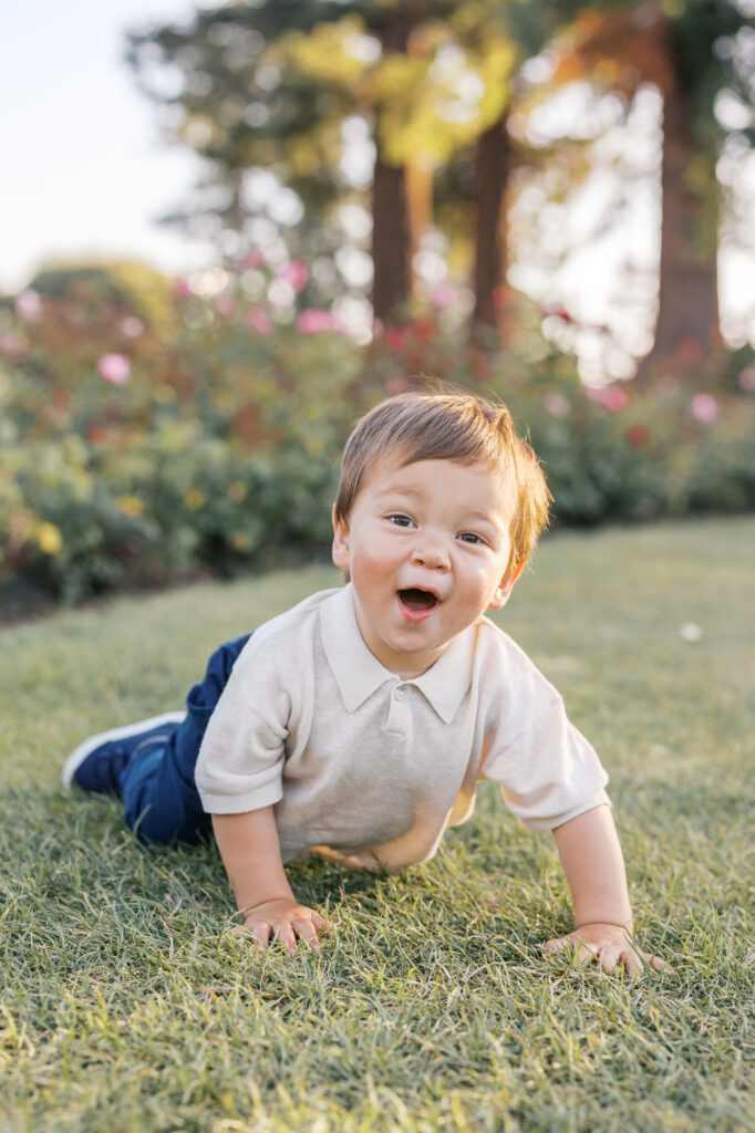 Young boy looks up at the camera smiling after falling from running during a San Jose Rose Garden photography session