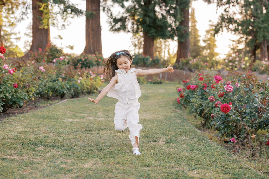 young girl happily runs thru the rows of roses at San Jose Rose Garden during golden hour