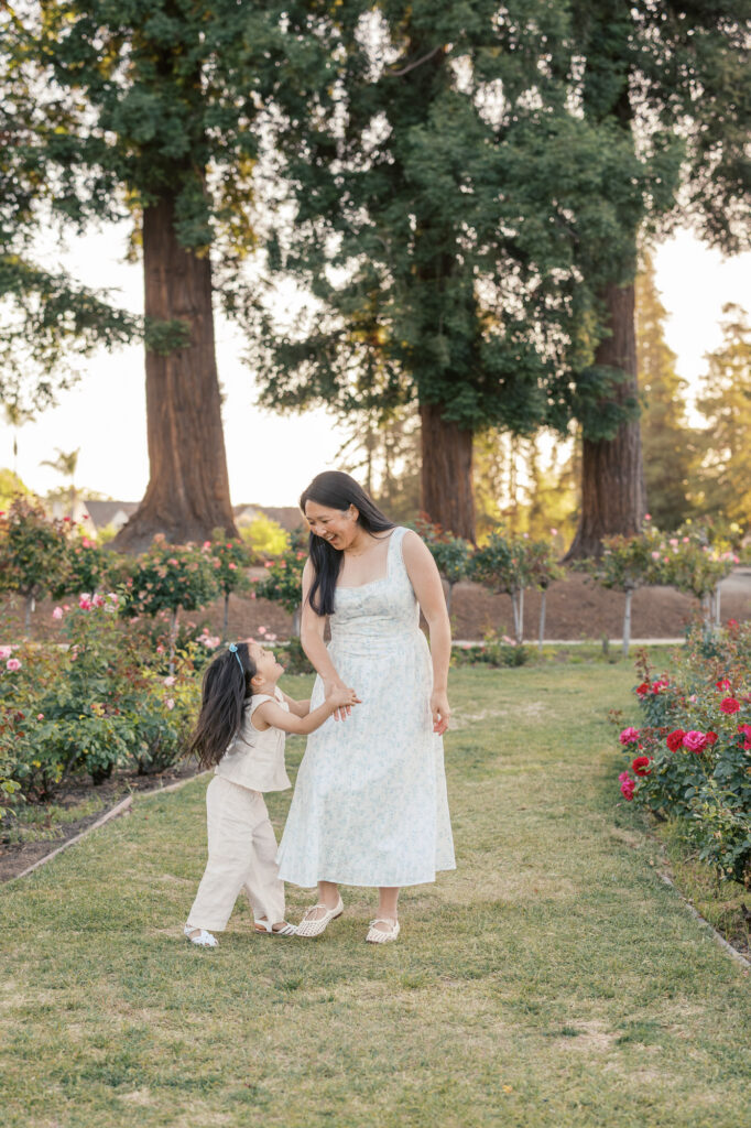 mother and young daughter laugh and play in the rows of San Jose rose garden during their Bay Area family photography session