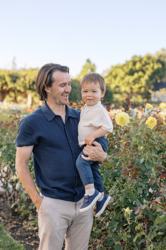 Father laughs while holding son in San Jose Rose Garden at golden hour